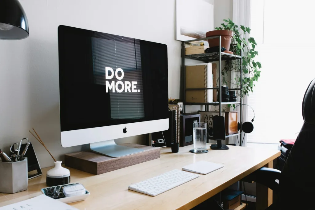 silver iMac with keyboard and trackpad inside room 'Do More' on screen