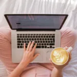 person typing on MacBook Pro and holding cappuccino