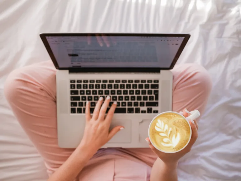 person typing on MacBook Pro and holding cappuccino